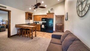 Une cuisine avec des meubles de rangement en bois, un réfrigérateur noir et un ventilateur de plafond.