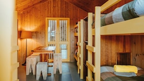 Quarto de cabana de madeira com beliches, uma mesa e um banco.