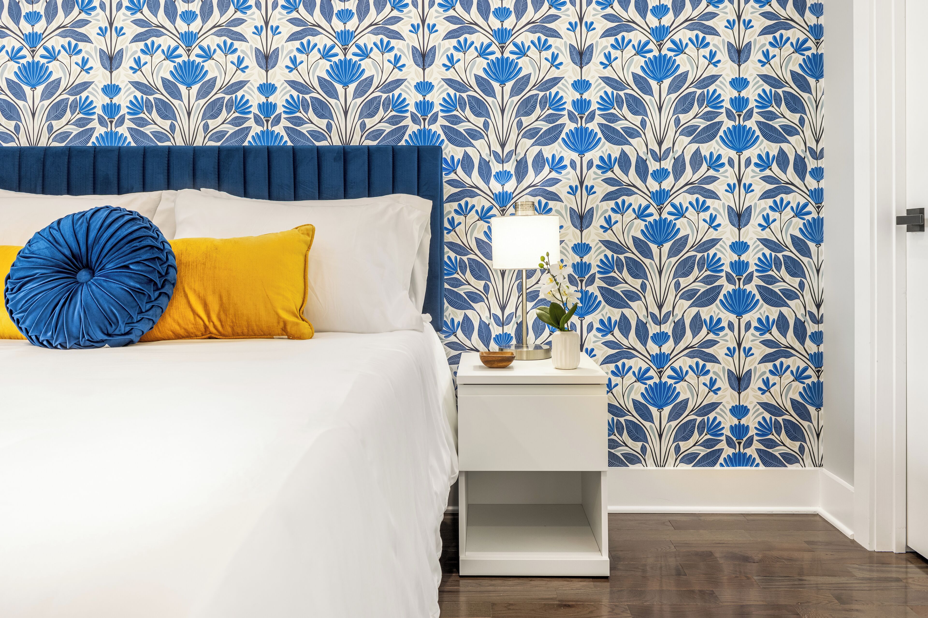 Ein Schlafzimmer mit einem Bett, einem Nachttisch und einer Wand mit blau-weißem Blumenmuster.