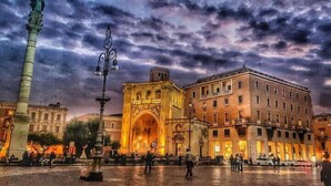 A historic square with a prominent archway, a tall column, and a building with multiple floors. - IL RIFUGIO DEI TEMPLARI (Lecce)