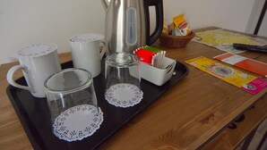 A tray with a kettle, mugs, glasses, and a basket of snacks on a wooden table. - IL RIFUGIO DEI TEMPLARI (Lecce)