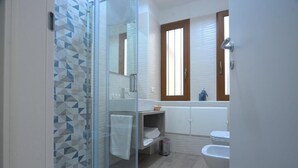 A bathroom with a glass shower enclosure, a white sink, a toilet, and a window with blinds. - IL RIFUGIO DEI TEMPLARI (Lecce)