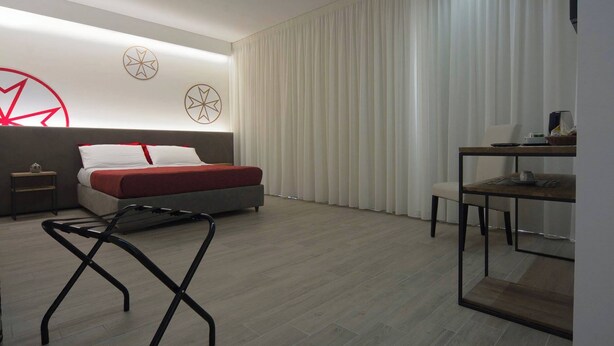 A modern hotel room with a bed, a desk, and a chair. There are two wall decorations and a large window with curtains. - IL RIFUGIO DEI TEMPLARI (Lecce)