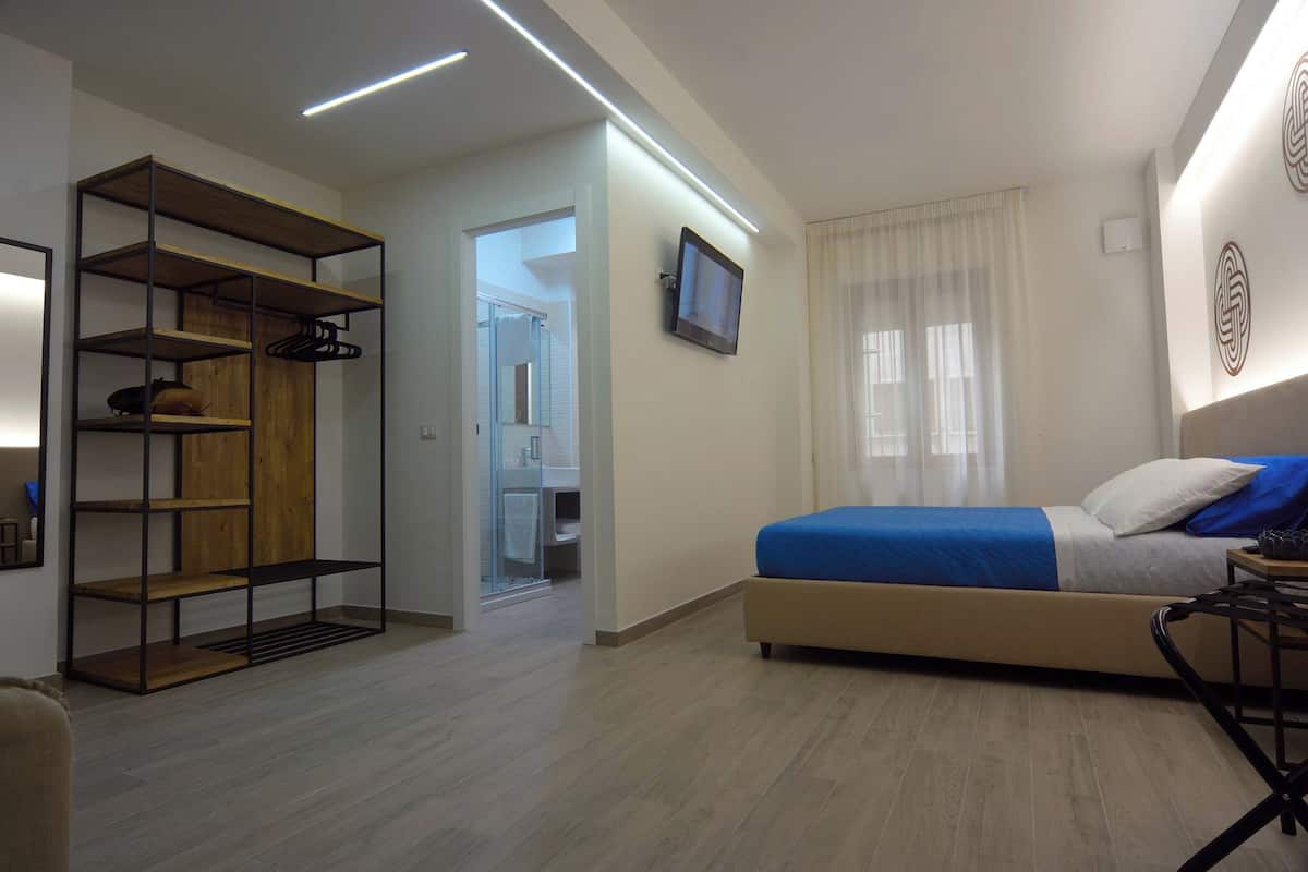 Une chambre à coucher avec un lit, une télévision, une armoire et une salle de bain visible à travers une porte ouverte.