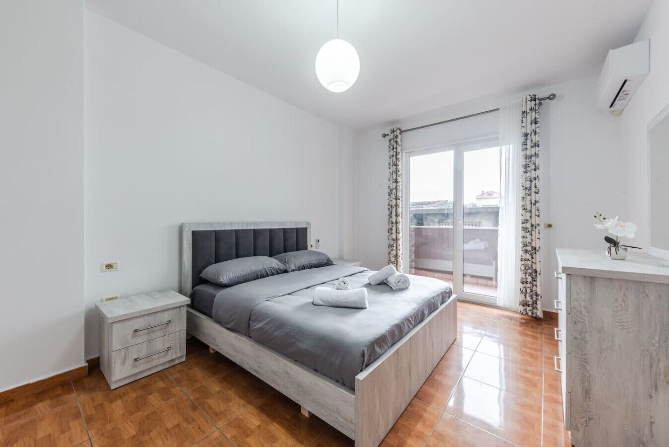 A bedroom with a bed, a nightstand, a dresser, and a window with curtains.