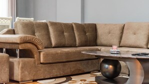 A brown sectional sofa with a matching ottoman, a round coffee table, and a patterned rug. - The Triple Comfort Loft by PikHost (Shkodër)