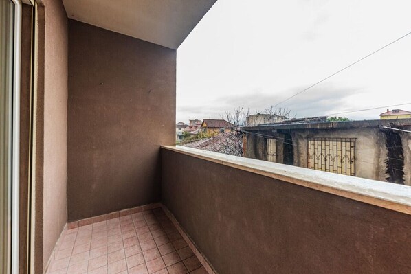 A balcony with a tiled floor, a concrete wall, and a view of neighboring buildings. - The Triple Comfort Loft by PikHost (Shkodër)