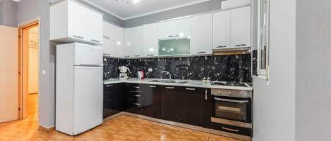 A modern kitchen with white cabinets, a black marble backsplash, and a wooden floor.