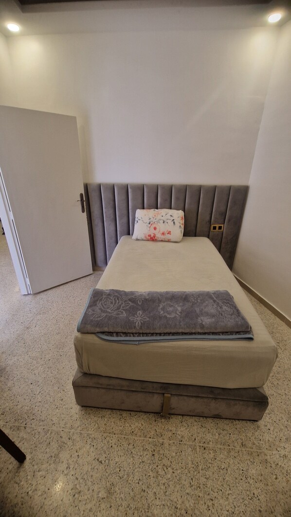 Un lit avec une tête de lit grise, un coussin à motifs floraux et une couverture grise.