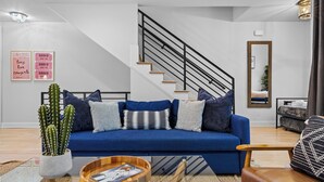 A modern living room with a blue sofa, a wooden coffee table, a cactus plant, and a staircase with black railings.
