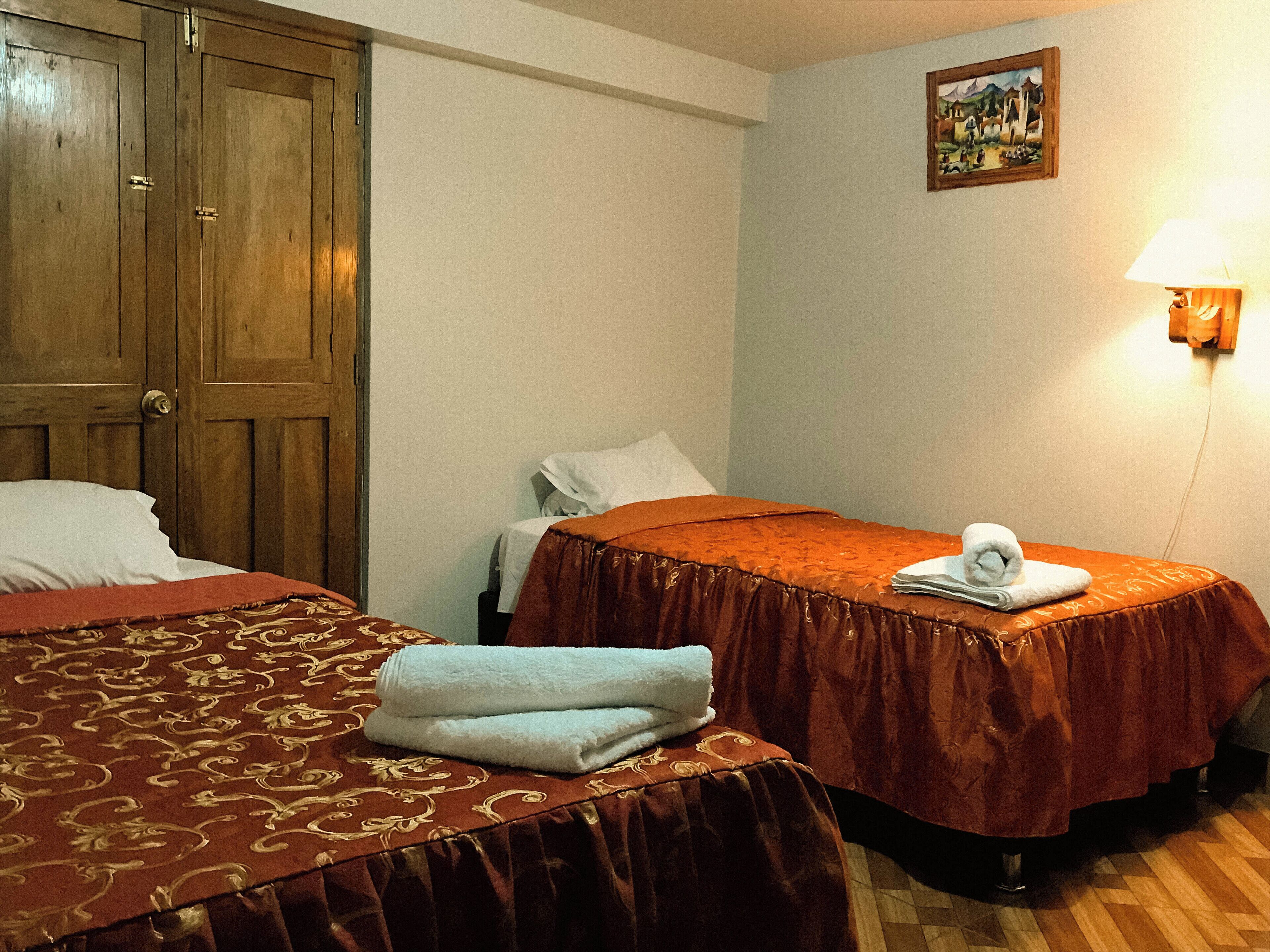 A hotel room with two beds, wooden wardrobe, a painting on the wall, and a lamp.