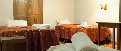 A hotel room with two beds, each with a red bedspread and white pillows. There is a wooden wardrobe and a painting on the wall.