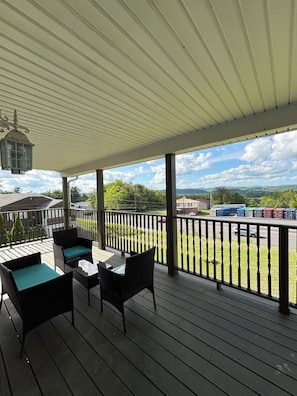 A covered outdoor deck with wicker furniture and a table, overlooking a parking area and distant landscape. -  Big house in lovely South Williamsport 600 yards from little league baseball (South Williamsport)