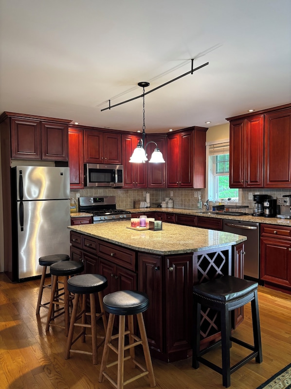 A modern kitchen with dark wood cabinets, stainless steel appliances, a granite countertop, and pendant lighting.