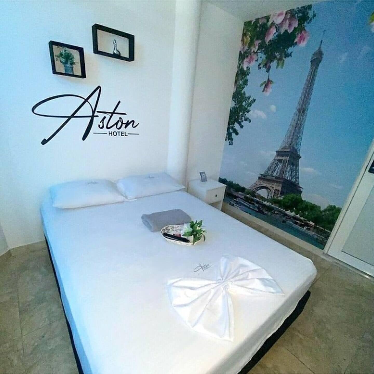 Habitación de hotel con cama, mesita de noche y una pared con una imagen de la Torre Eiffel.