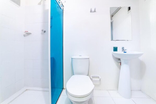 Un baño con inodoro blanco, lavabo y zona de ducha.