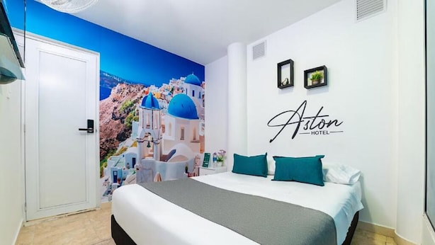 A hotel room with a bed, a wall mural of a coastal scene, and the hotel's name on the wall. - Hotel Aston Cúcuta (San José de Cúcuta)