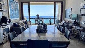 A modern dining area with a large table, chairs, and a view of the ocean.