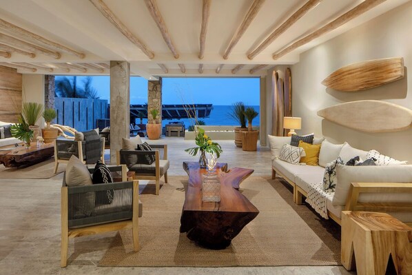 Amplia sala de estar con vista al océano, que incluye una mesa de centro de madera, sofás y plantas en macetas.