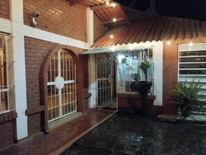 Un patio con un edificio de ladrillo, una zona cubierta con luces colgantes y plantas en macetas.