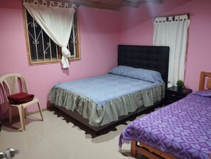 Un dormitorio con una cama individual, una silla, una mesita y un ventanal con cortinas.
