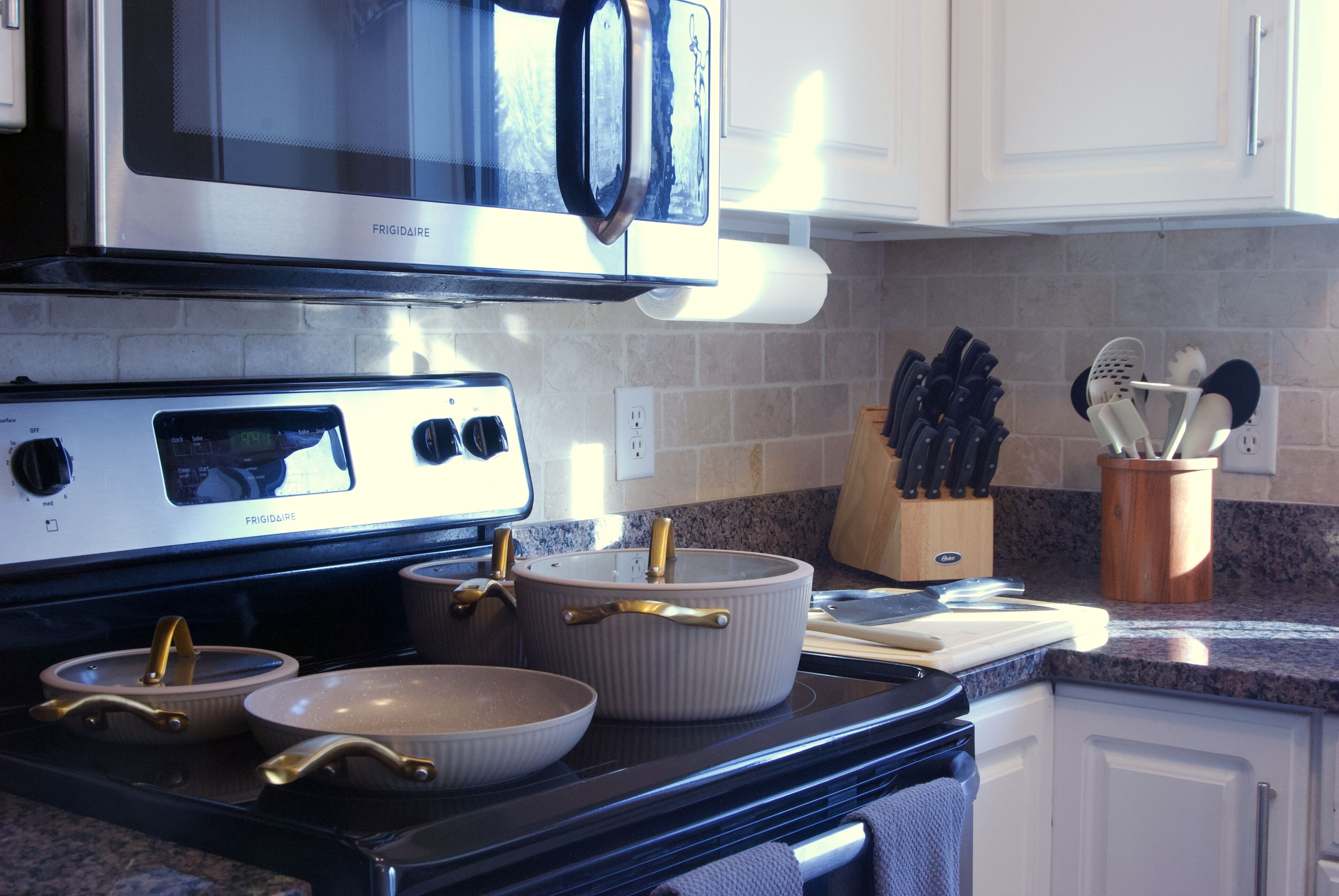 A kitchen with a stove, pots, a microwave, and a knife block.