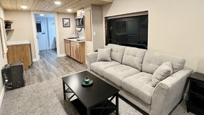 A compact living space with a sofa, a coffee table, a kitchen area, and a doorway leading to another room. - Cherrywood lane train #2 (Seward)