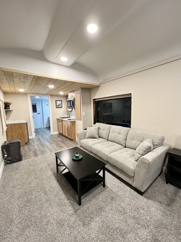 A compact living space with a sofa, a coffee table, a kitchen area, and a doorway leading to another room.