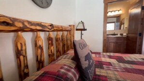 Une chambre à coucher avec une tête de lit en bois, une couvre-lit à carreaux et un coussin orné d’un motif représentant un ours.