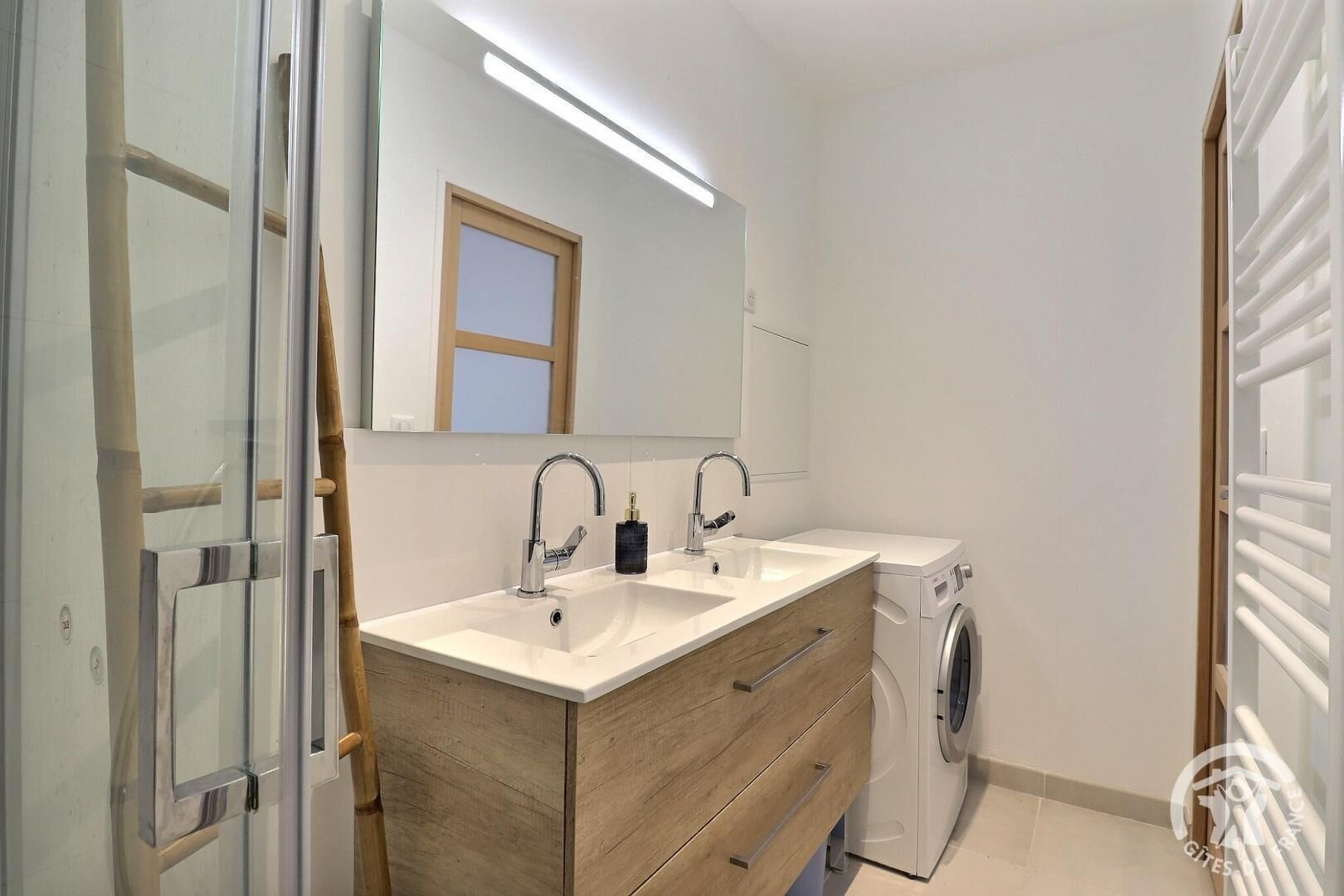 Une salle de bain moderne avec deux lavabos, un miroir, un lave-linge et un meuble en bois.