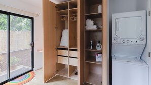 Una habitación con un armario de madera, lavadora y puerta de vidrio corredera que da a un balcón con planta en maceta.