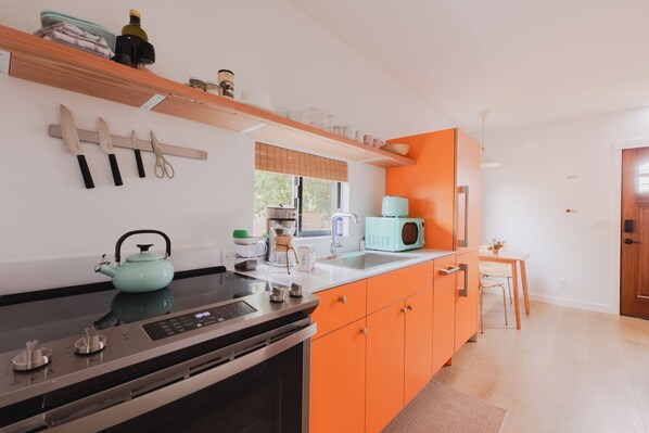 Une cuisine moderne avec un poêle noir, des armoires orange et une bouilloire turquoise.