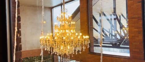 A large, ornate chandelier hanging in a room with large windows and a brick wall.