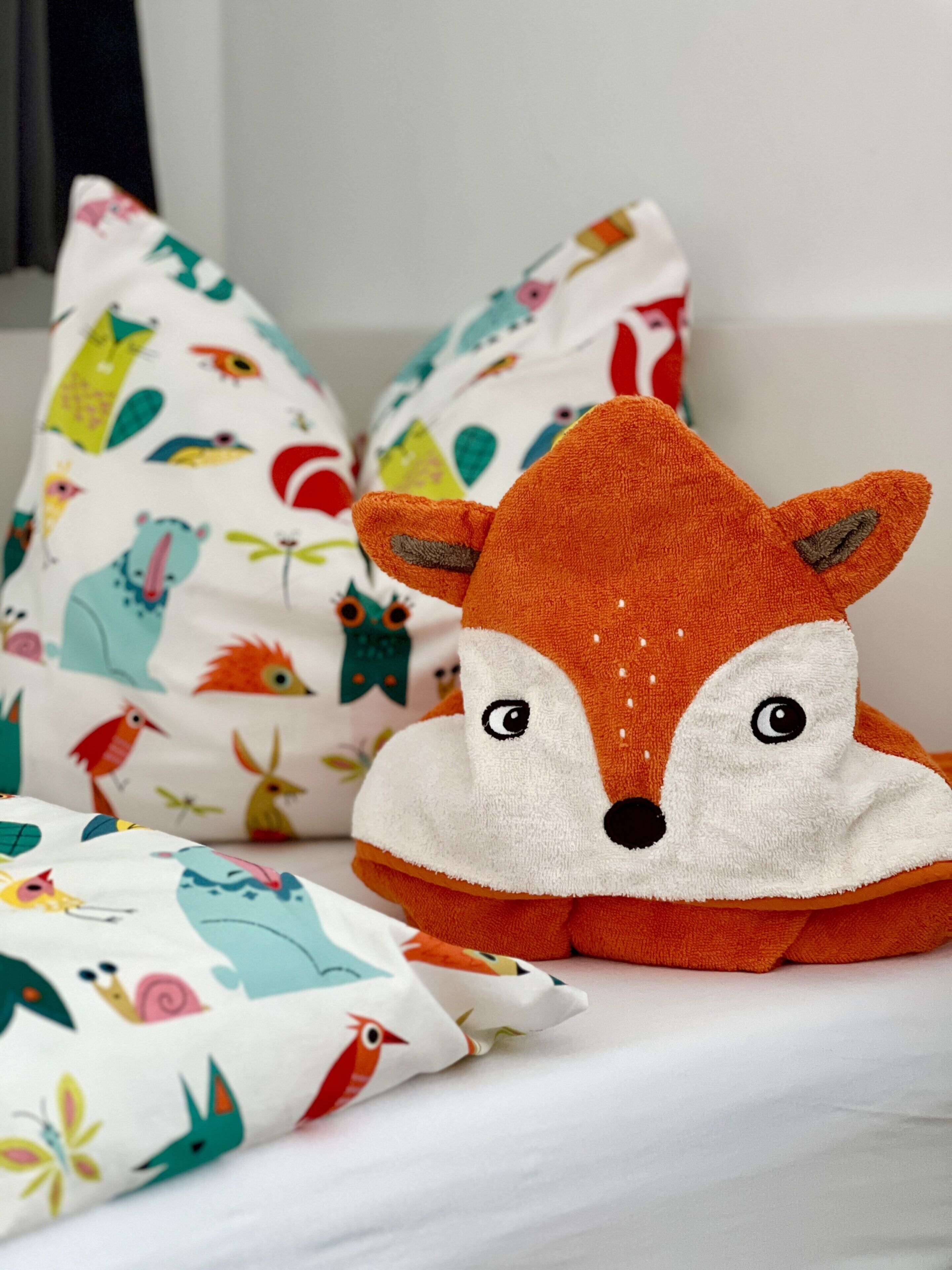 A plush toy fox on a bed with colorful pillows featuring animal prints.