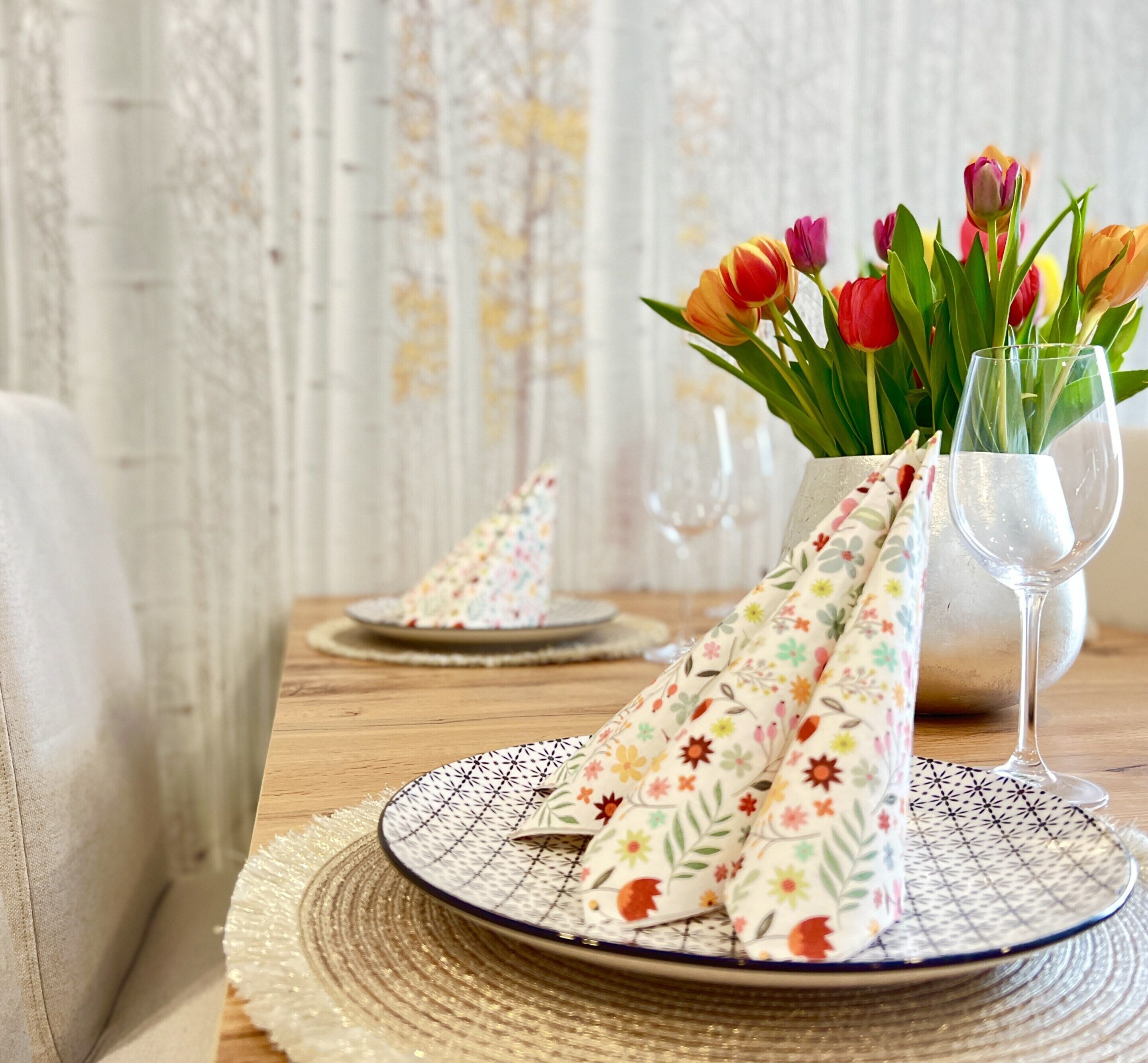 Ett matbord dukat med blommiga servetter, en vas med tulpaner och ett vinglas.