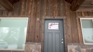 A wooden cabin with a stone foundation, a gray door, and a number '3' on the wall. - King Room at Ponds Lodge Cabin 6 Unit 3 (Island Park)