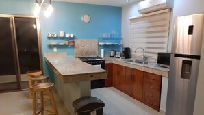 Une cuisine moderne avec un plan de travail en granit, des tabourets en bois, un réfrigérateur en acier inoxydable et une horloge murale.