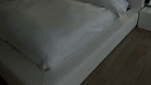 Een netjes opgemaakt bed met witte lakens, een hoofdbord met ingebouwde verlichting en een nachtkastje met een lamp.