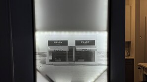 Een inlijsting toont een modern gebouw met 'PRADA'-aanduiding, een deur en een klein verlicht object eronder.