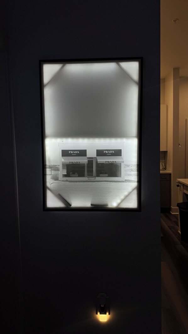 A framed view of a modern building with 'PRADA' signage, a door, and a small illuminated object below.