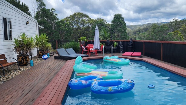 A swimming pool with inflatable rings, a wooden deck, and a view of the surrounding forest.