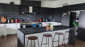 A modern kitchen with dark cabinetry, a marble countertop, and a central island with stools.