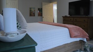 A bedroom with a bed, a wooden dresser, a television, and a painting on the wall.