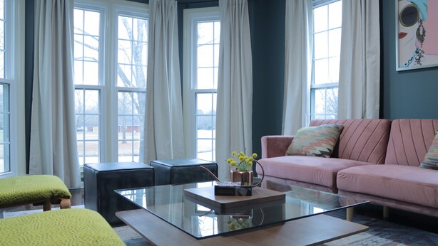 A living room with a glass coffee table, a pink sofa, and a green armchair.