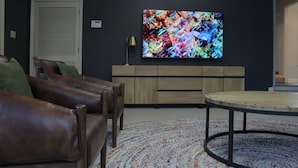A living room with a large TV, leather sofas, a wooden cabinet, and a round coffee table.