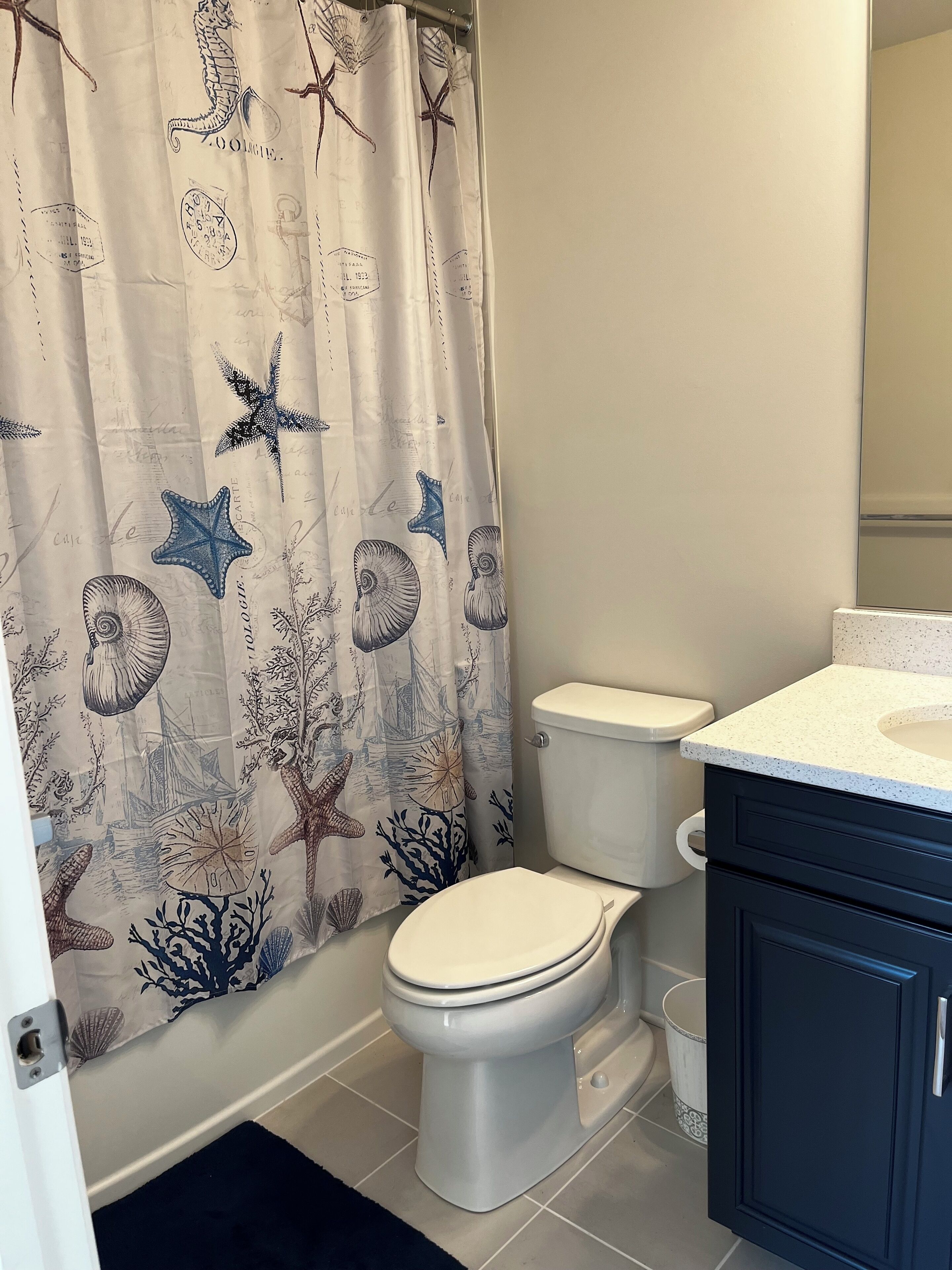 A bathroom with a toilet, a sink, and a shower curtain with a sea-themed design.