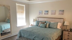 A bedroom with a large bed, a bench, a nightstand, a mirror, and artwork on the wall. - NEW - Spacious 4-bedroom near Bethany Beach in Bishops Landing resort + shuttle (Millville)