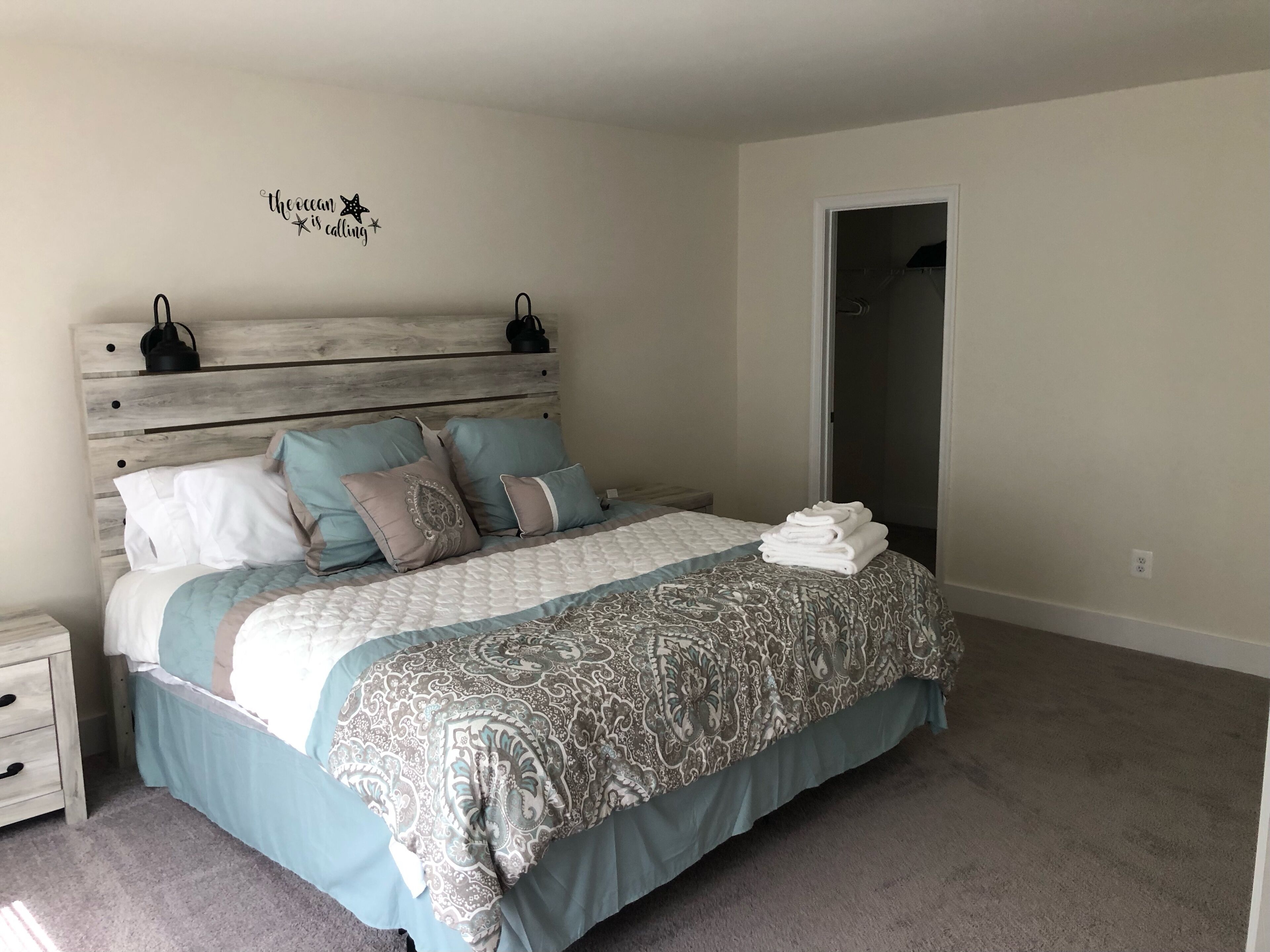 Un dormitorio con cabecera de madera, cama con ropa de cama estampada, mesita de noche y decoración en la pared.