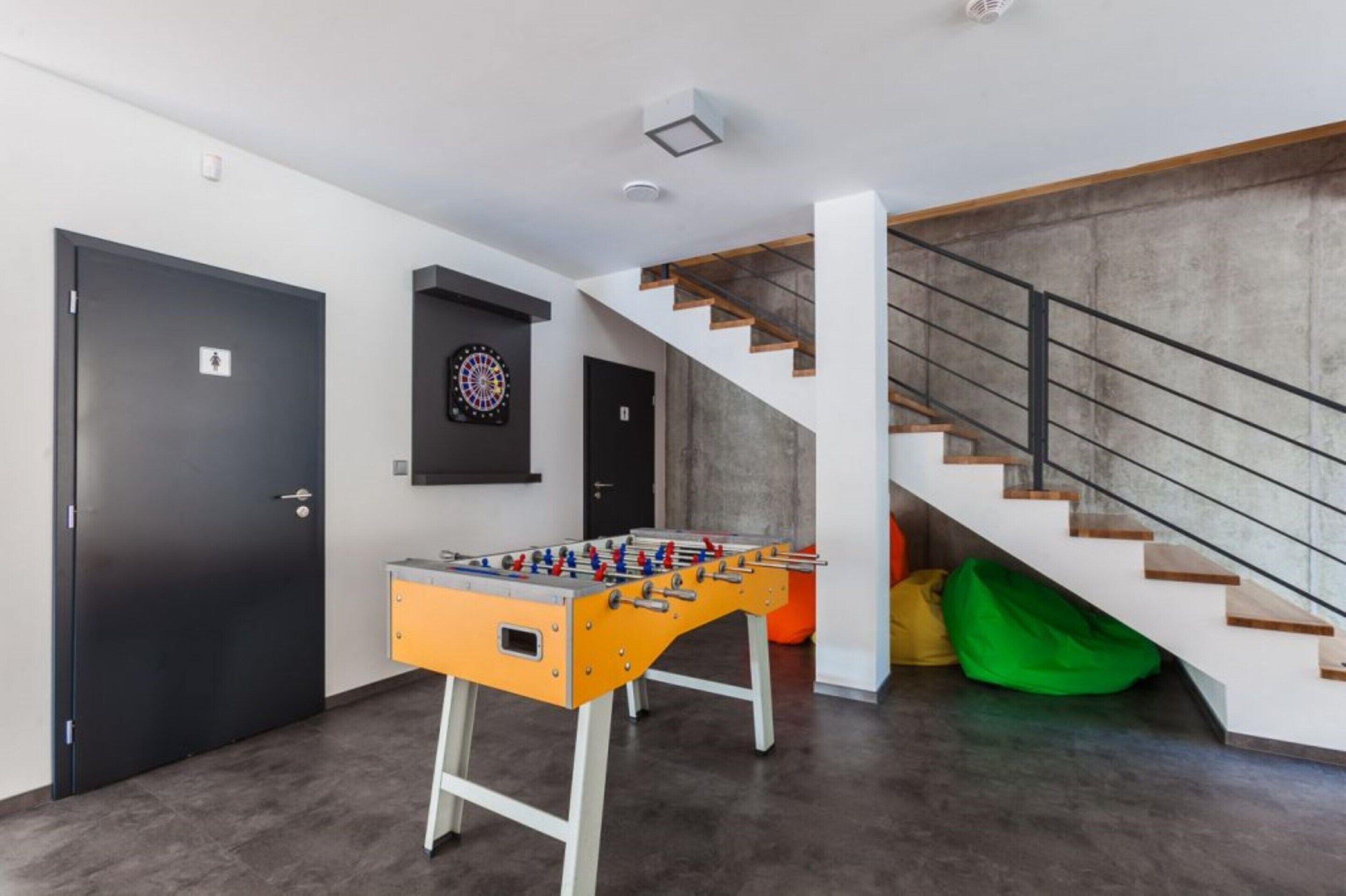 A modern room with a foosball table, a dartboard, and a staircase.