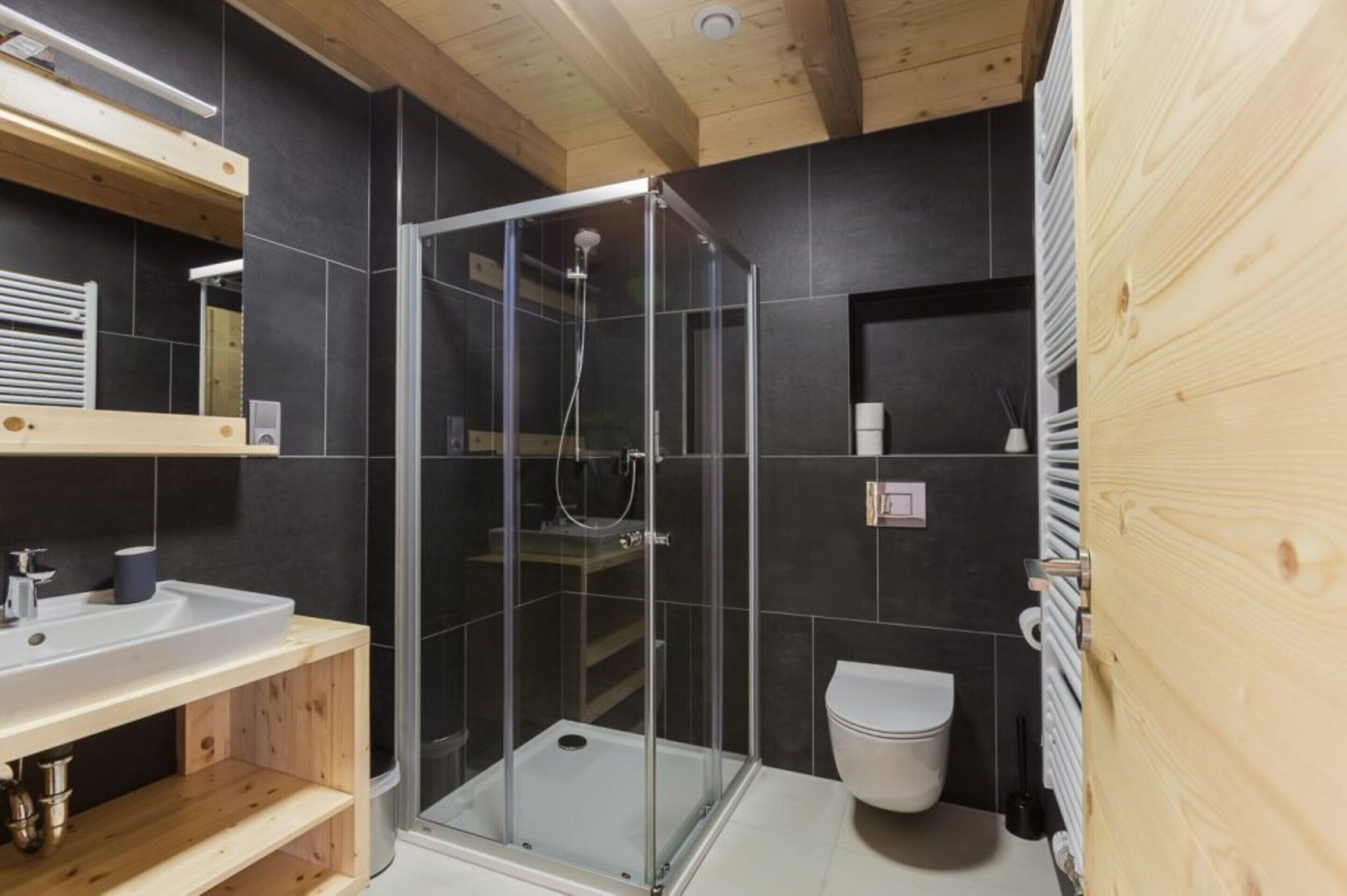 A modern bathroom with a glass-enclosed shower, a wooden vanity, and a white toilet.